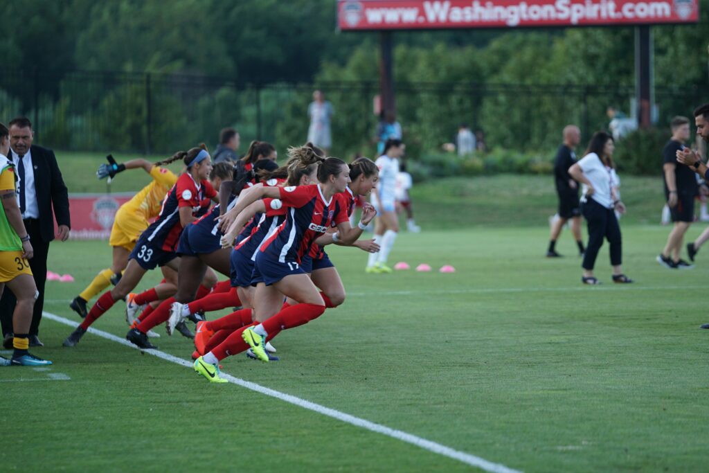A group of a female soccer team doing running drills during a match day on a green grass: Soccer Strength Training Exercises