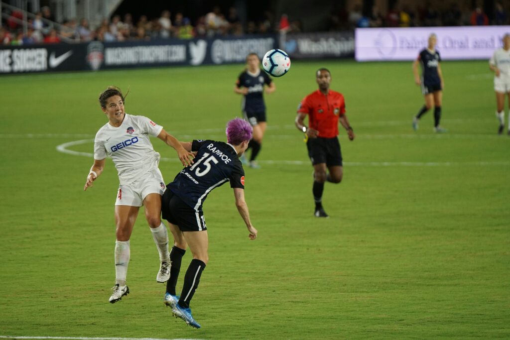 Megan Rapinoe alongside an opponent trying to win a soccer ball