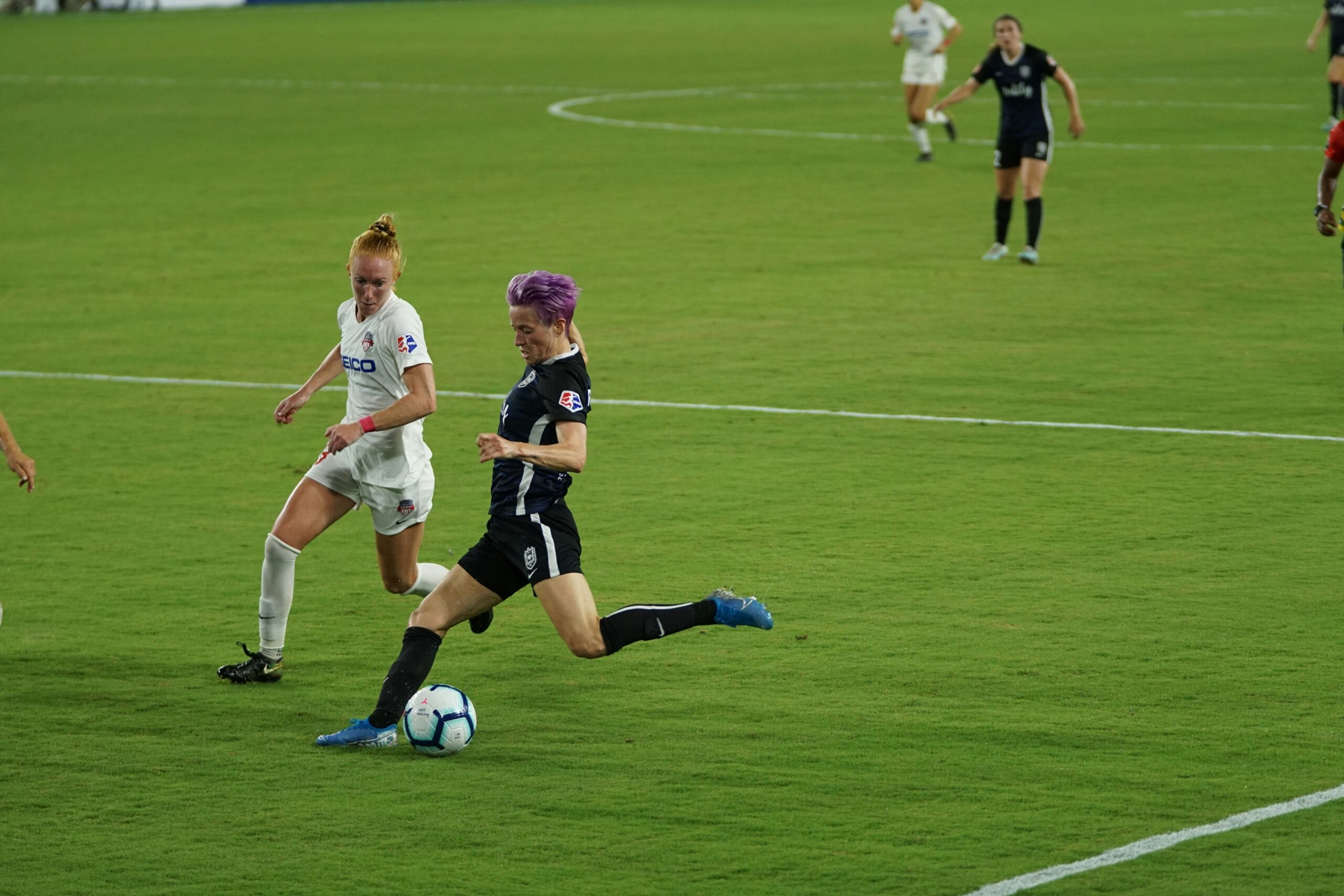 Megan Rapinoe trying to shoot a ball during game day alongside her opponent