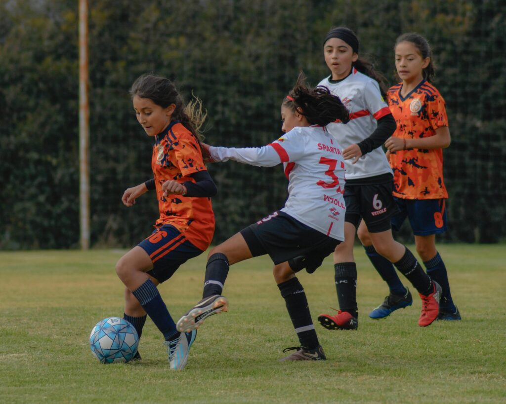 Two soccer girls on a soccer field with one trying to do a reckless tackle from behind