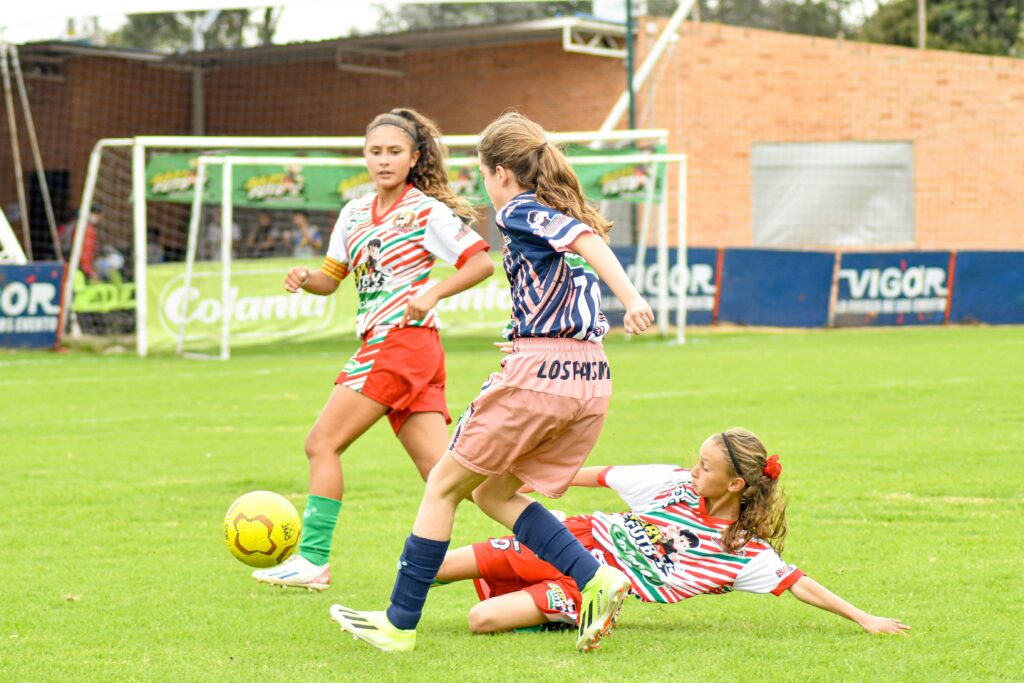 a group of soccer girls playing soccer on a field with one doing a clean tackle