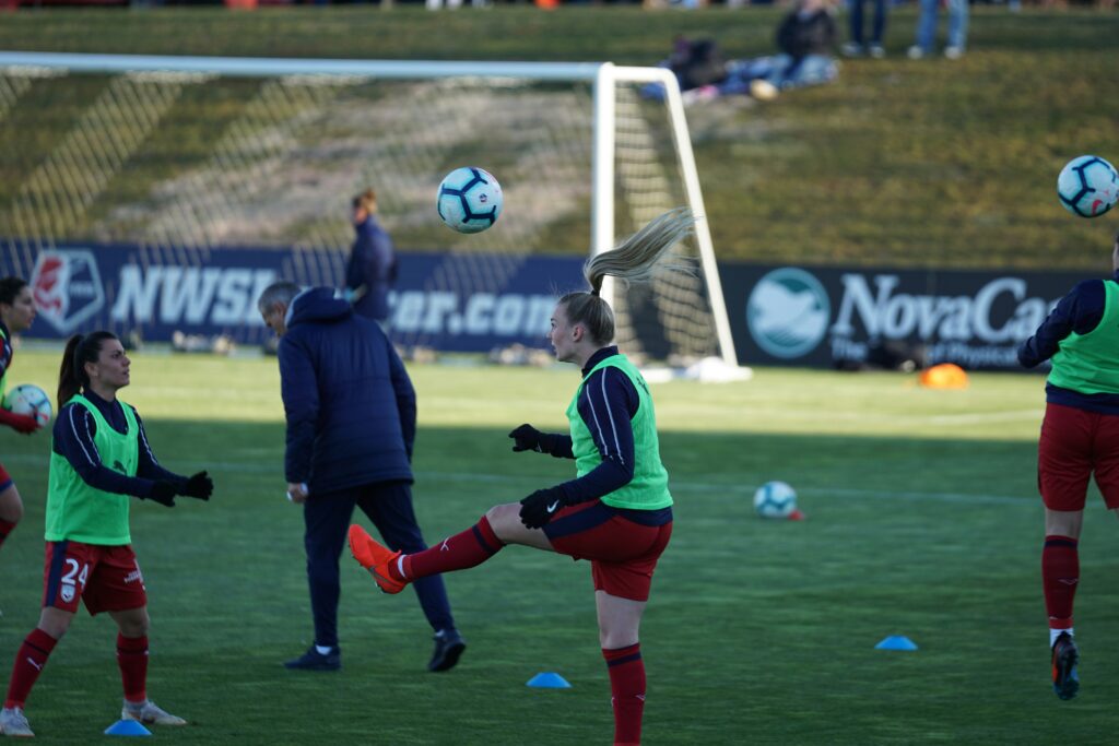 Two female footballers on a green pitch during a training section, training soccer headers