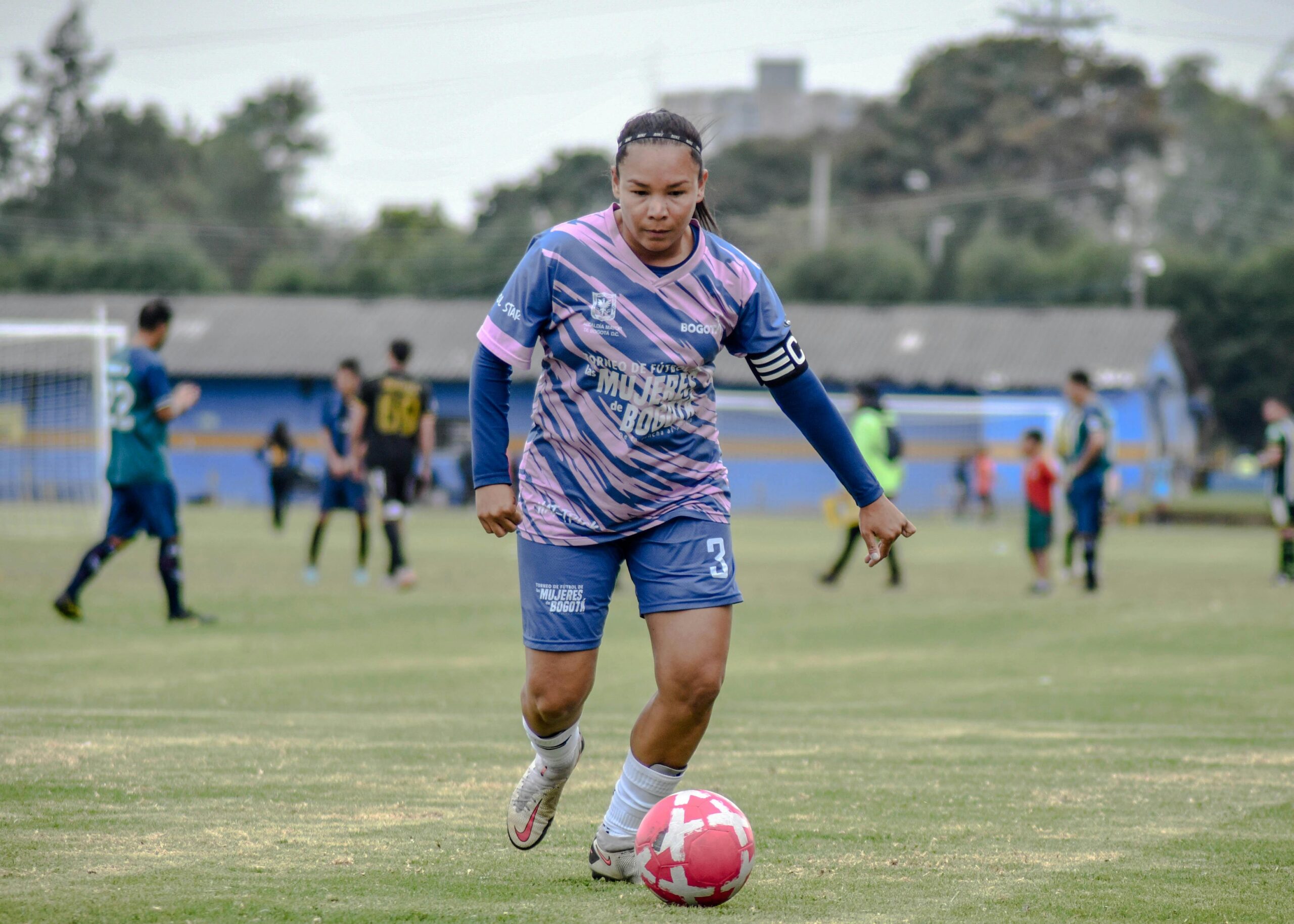 A female soccer player wearing a captain armband in action on a soccer green pitch: Female Soccer Captain