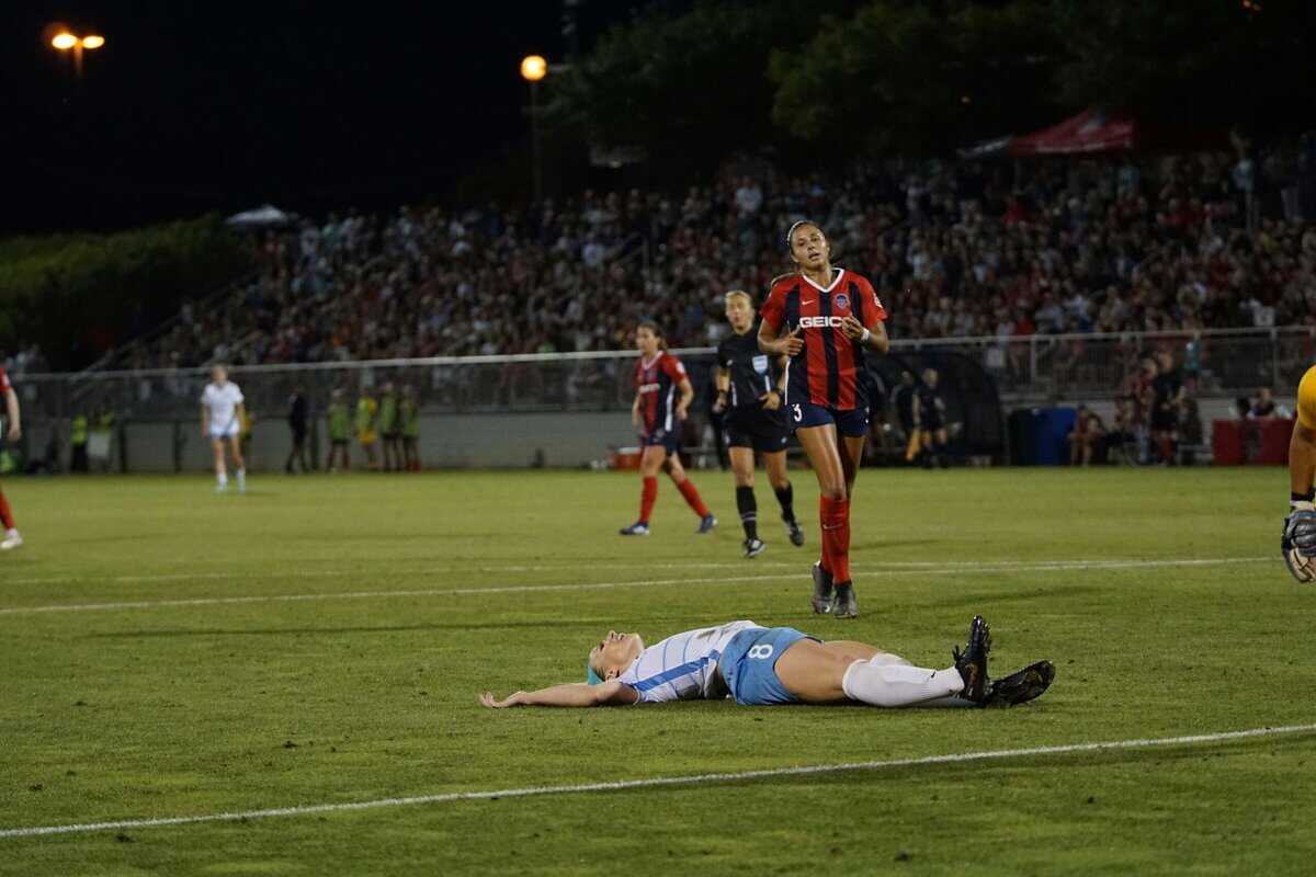 A frustrated women soccer player lying on a green pitch during a match day alongside a chasing oppenent: Setbacks in Soccer