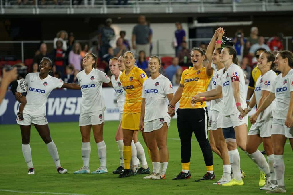 A group of female soccer players celebrating while holding hands on a green soccer field during daytime: Setbacks in Soccer