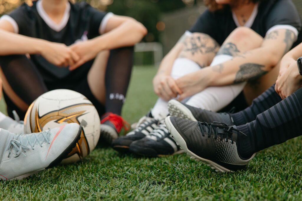 Women soccer players sitting on green grass showing their soccer cleats: Matchday Soccer Bag