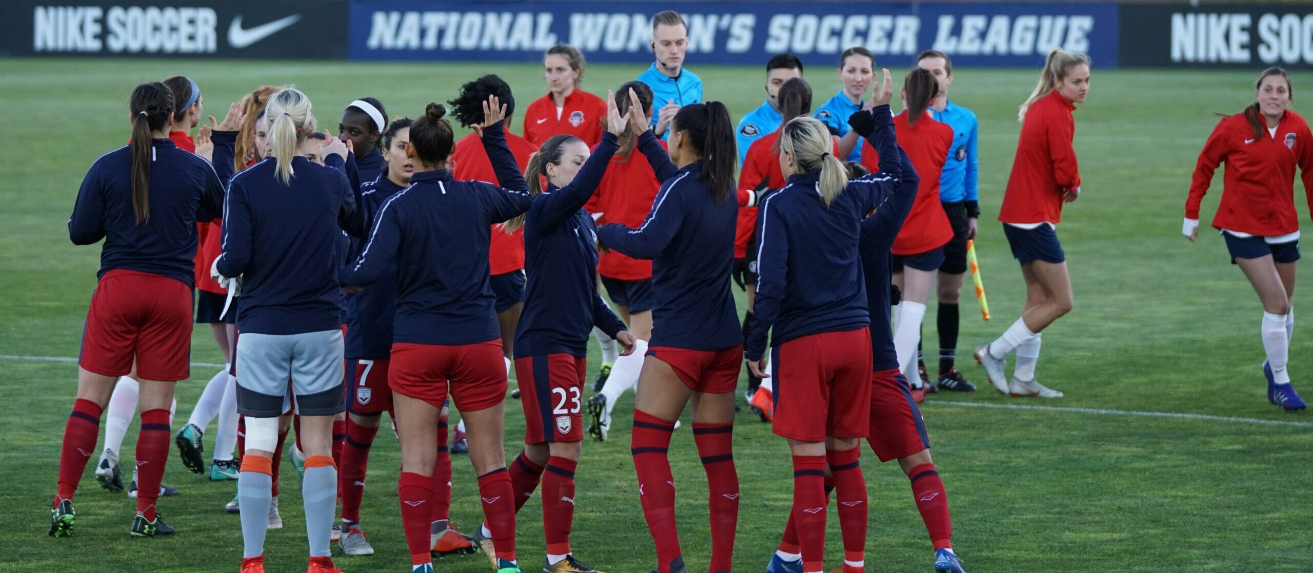 A group of women soccer players standing on a green pitch alongside soccer referees on a women's football matchday: soccer career opportunities for women
