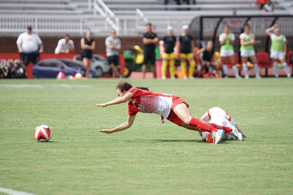 Two female soccer players one wearing a red and the other white jersey on a green soccer pitch during daytime: how to become a pro female soccer player