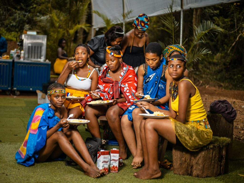 A group of beautiful African girls wearing cultural costumes sitting on a bench while eating