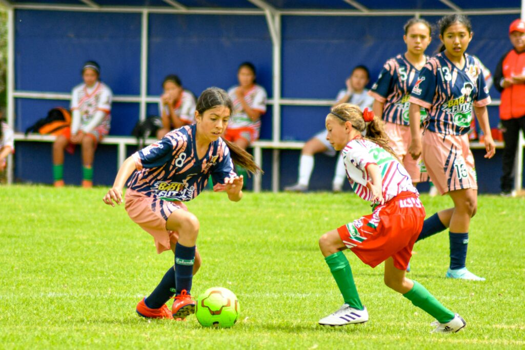 Soccer girls playing soccer on a green soccer pitch during day time nutmeg in women's soccer